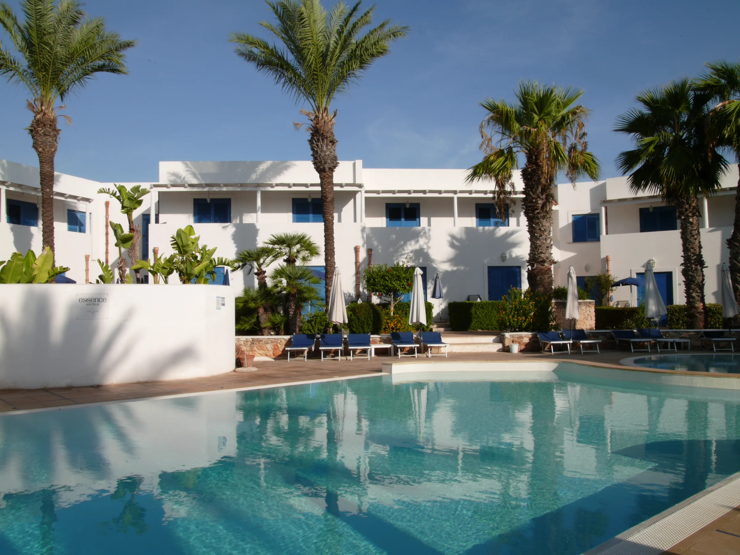 Cortile di Cala La Luna Resort con palme, piscina e persiane blu